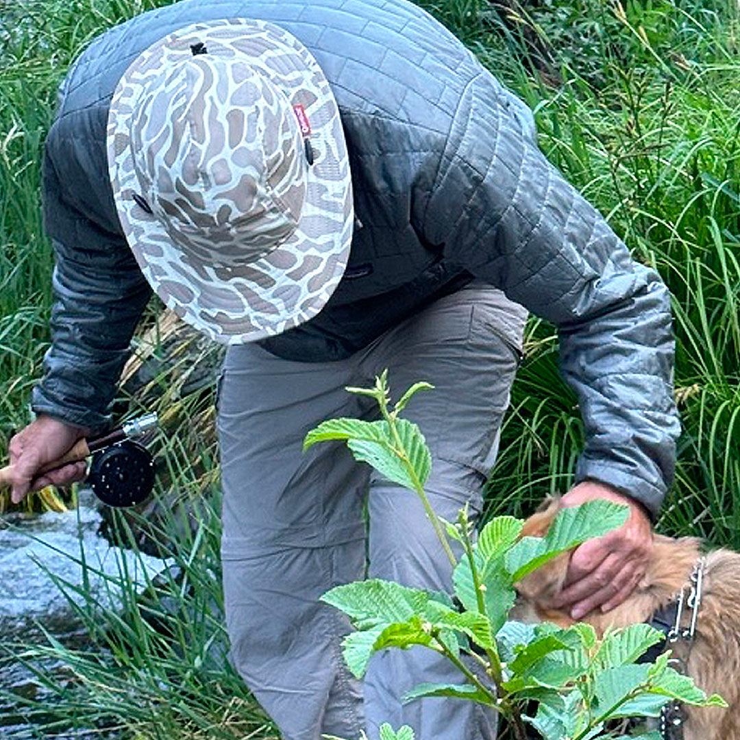 Person in outdoor gear with a dog by a stream