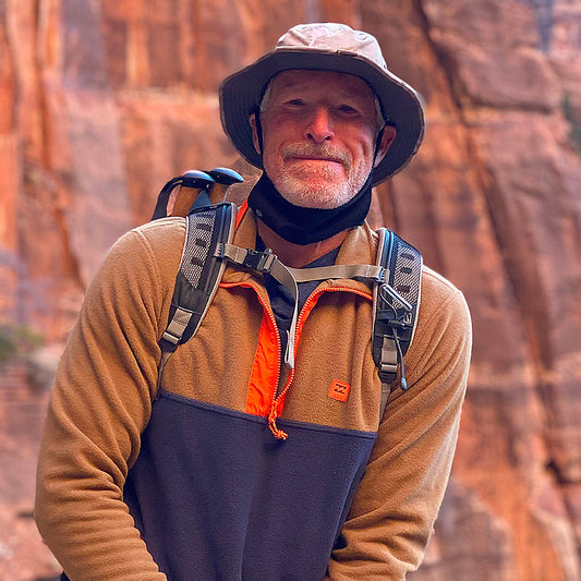 Man with a backpack standing in front of a rocky cliff