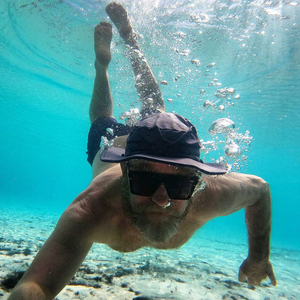 a man completely under water with a shelta seahawk sun hat on