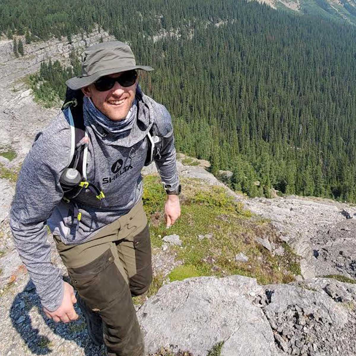a man backpacking in the canadian wilderness wearing a shelta hat and assault hoodie