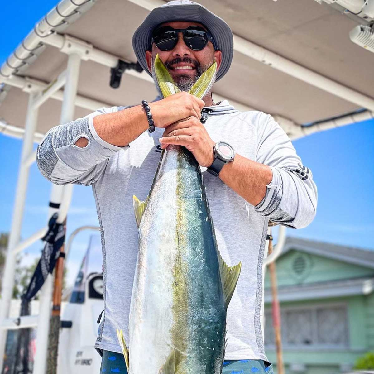 a man holding up a yellowfin tuna he just caught wearing a shelta sun hat and assault hoodie