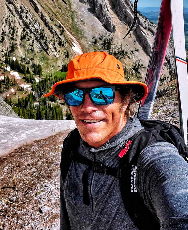 Person with skis on a mountain, wearing an orange cap and sunglasses