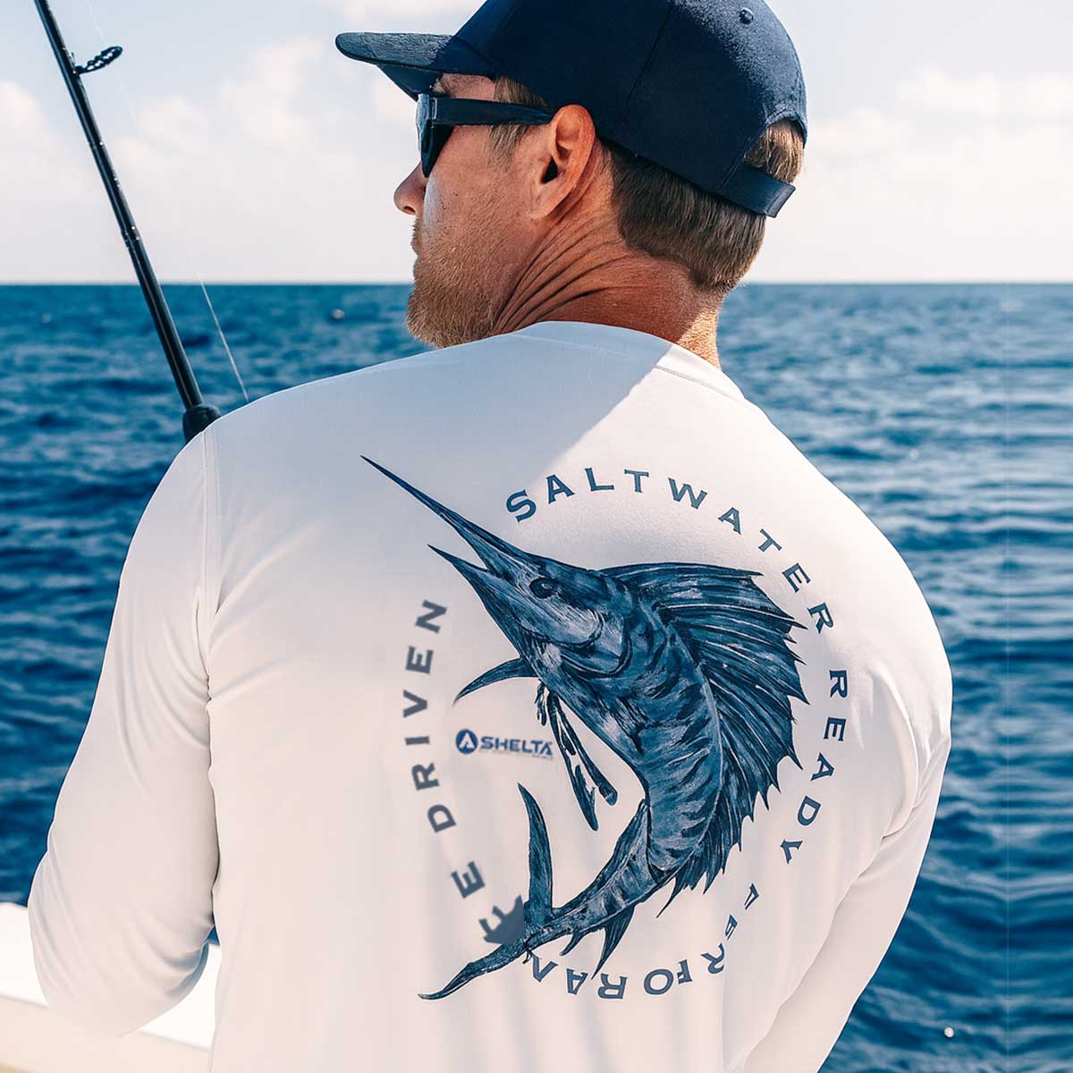Man wearing a 'Saltwater Ready' shirt with a fish design by the ocean.