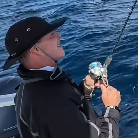 a man realing in a fish while wearing a shelta sunhat in black ops