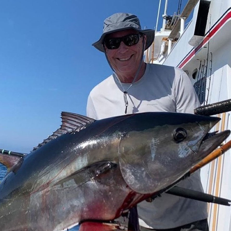 a man holding a huge tuna he caught while wearing a shelta sun hat