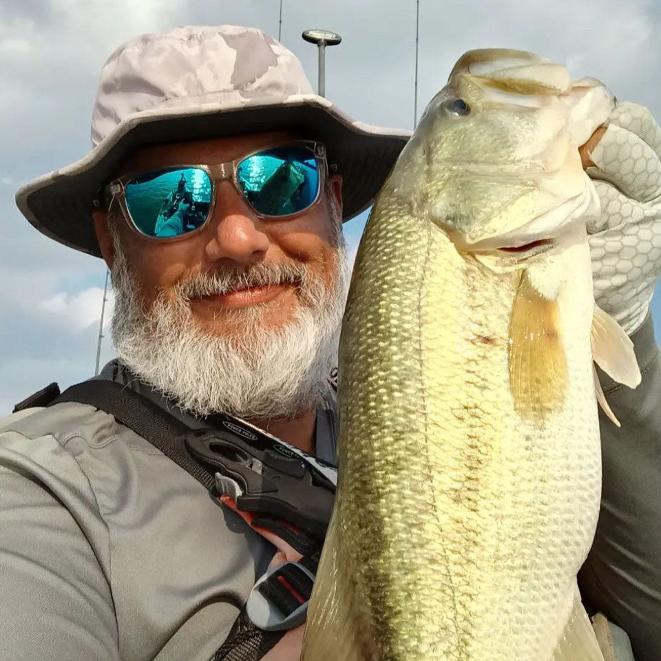 a man holding up a huge bass he just caught wearing a shelta sun hat