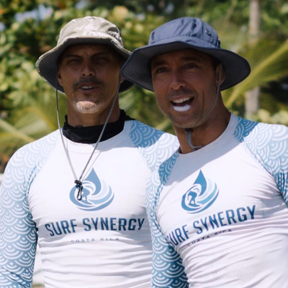 two surfers in rashguards and shelta hats observing a surf contest