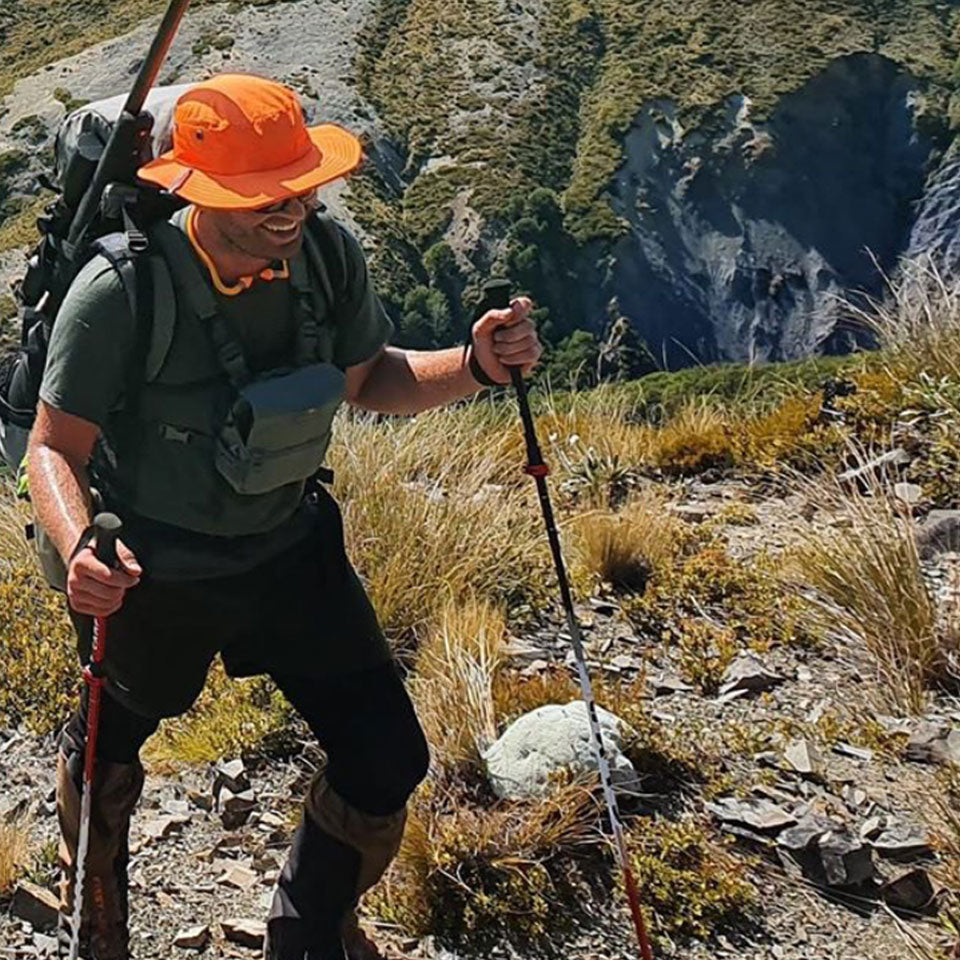 a man hiking a rugged trail while hunting in the wild wearing a orange shelta sun hat
