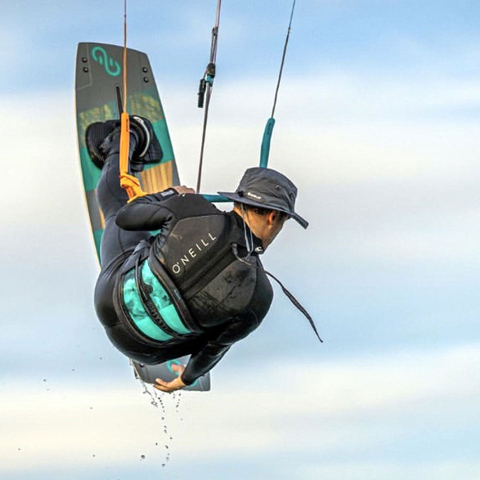 a man high in the air while kite boarding and wearing a shelta sun hat