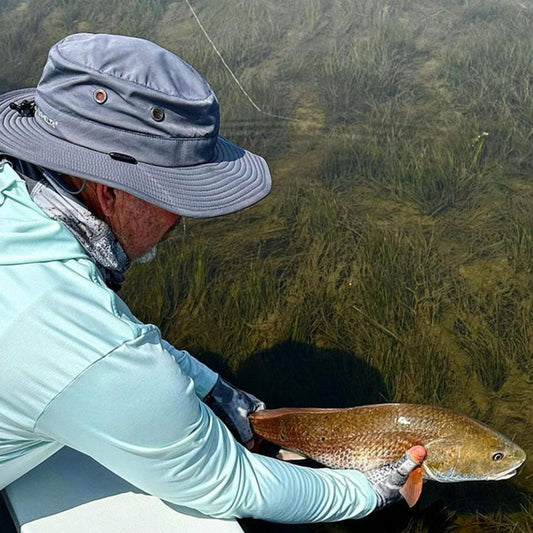 a man releasing a fish he caught while wearing a shelta sun hat