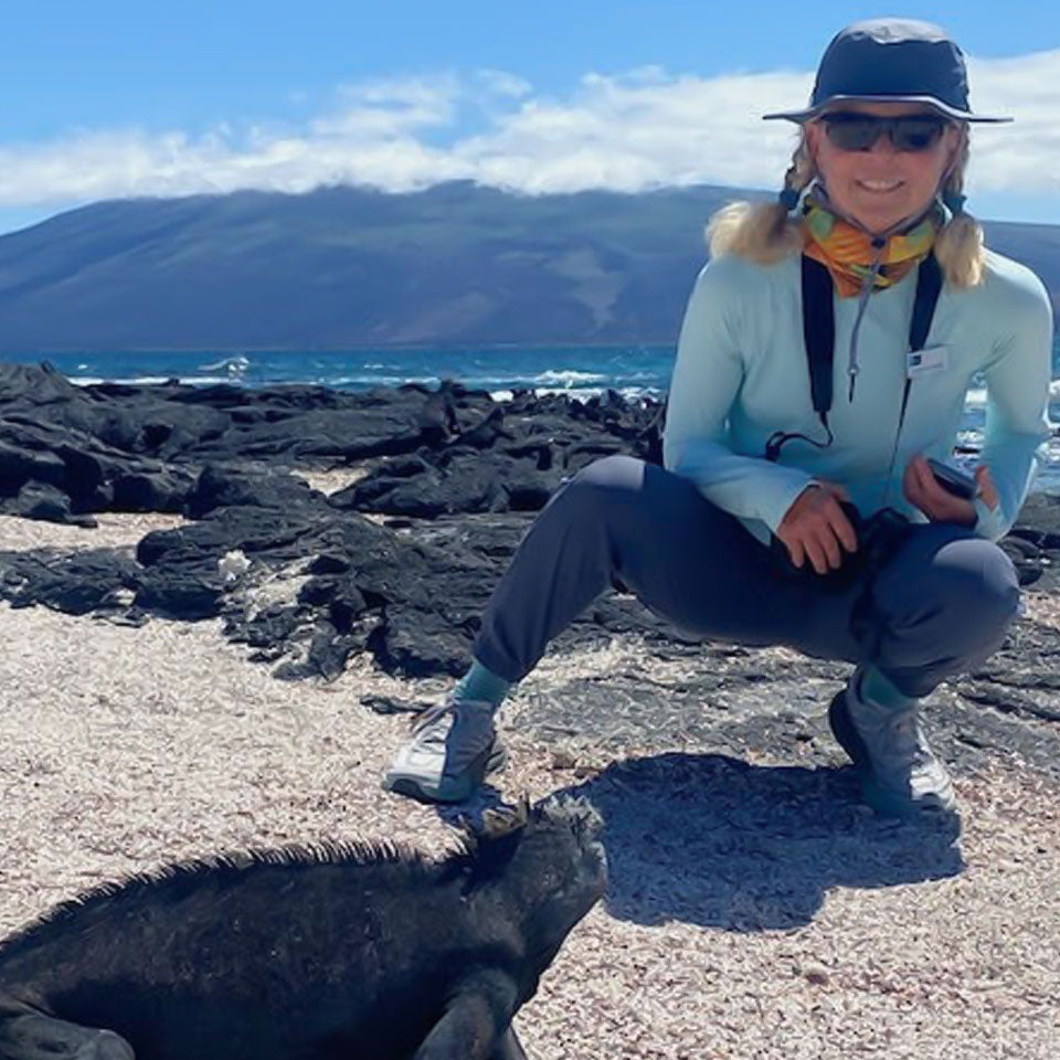 a women observing a dragon lizard on the galapegos islands wearing a shelta sun hat