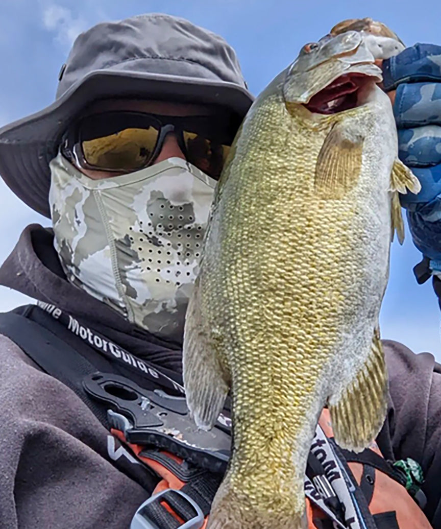 Man wearing shelta hat and face gaiter holding fish
