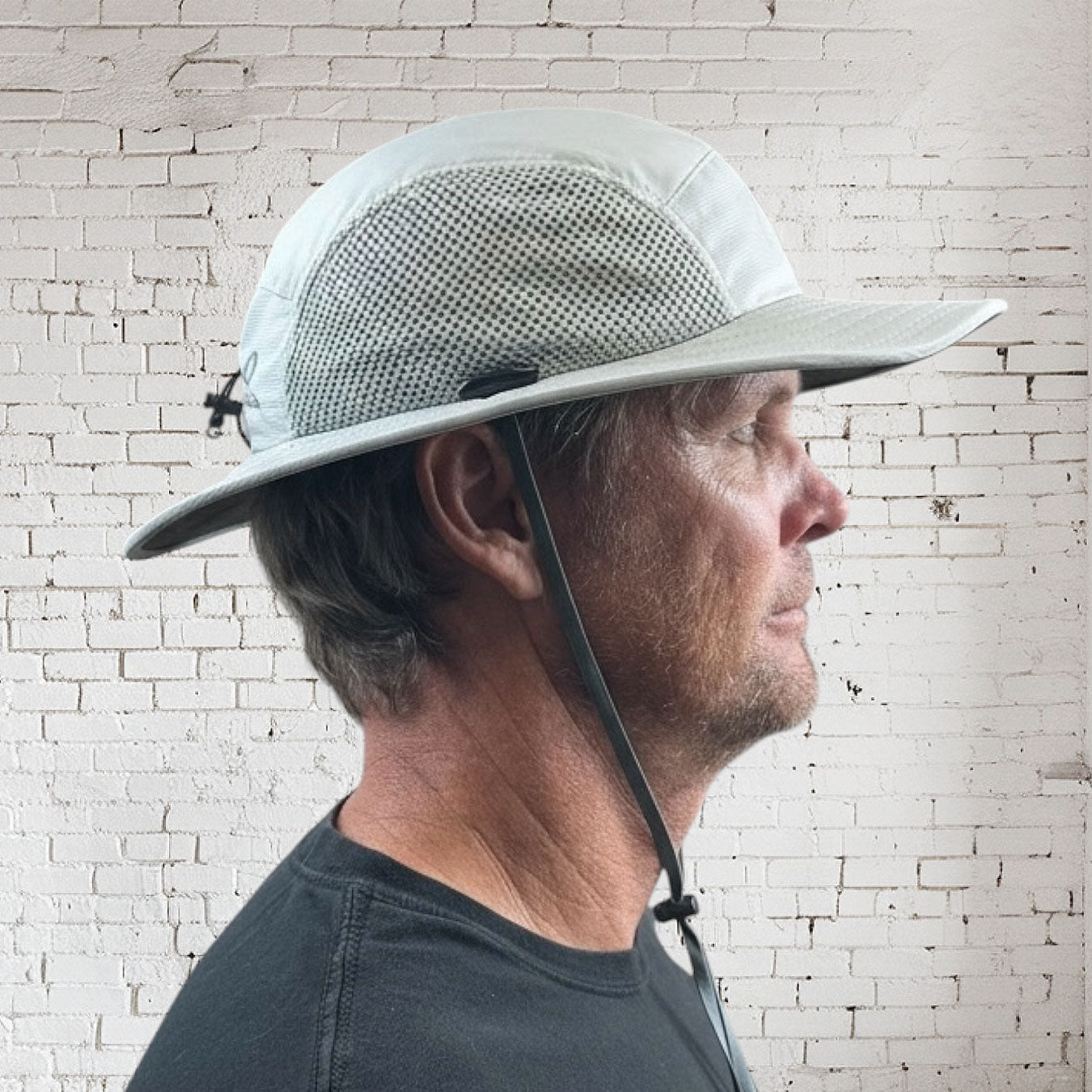 Man wearing a wide-brimmed hat against a white brick wall