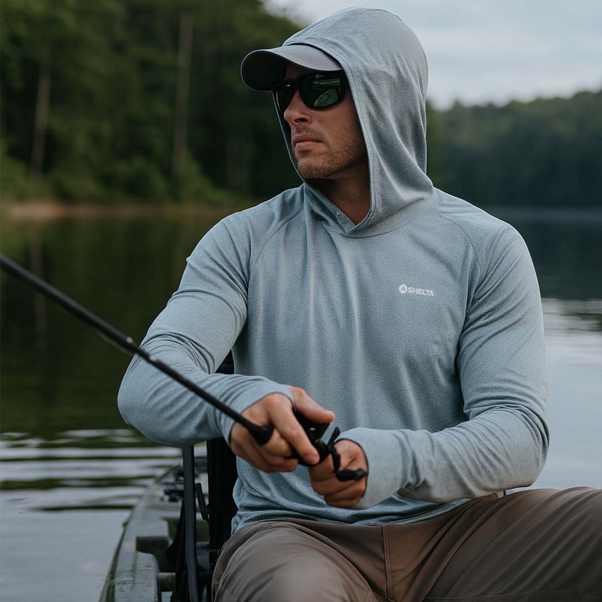 Man fishing on a dock wearing a hooded shirt with a brand logo.