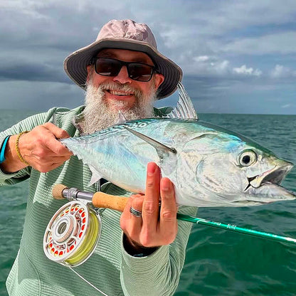 Man holding a large fish caught with a fly fishing rod on a body of water.