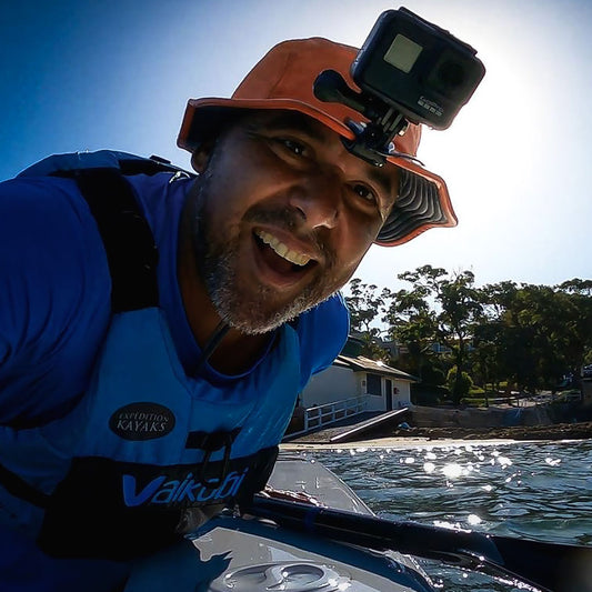 Man on a kayak with a GoPro camera, wearing a blue life jacket and orange shelta sun hat