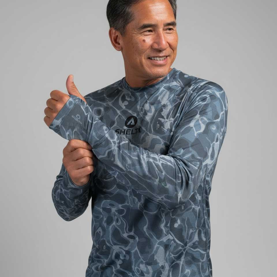 Man wearing a blue camouflage-patterned shirt with a brand logo, giving a thumbs-up gesture on a gray background.