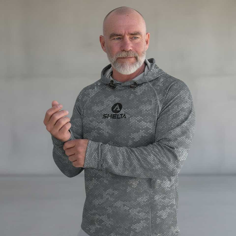 Man wearing a gray camouflage hoodie with a brand logo on a plain background