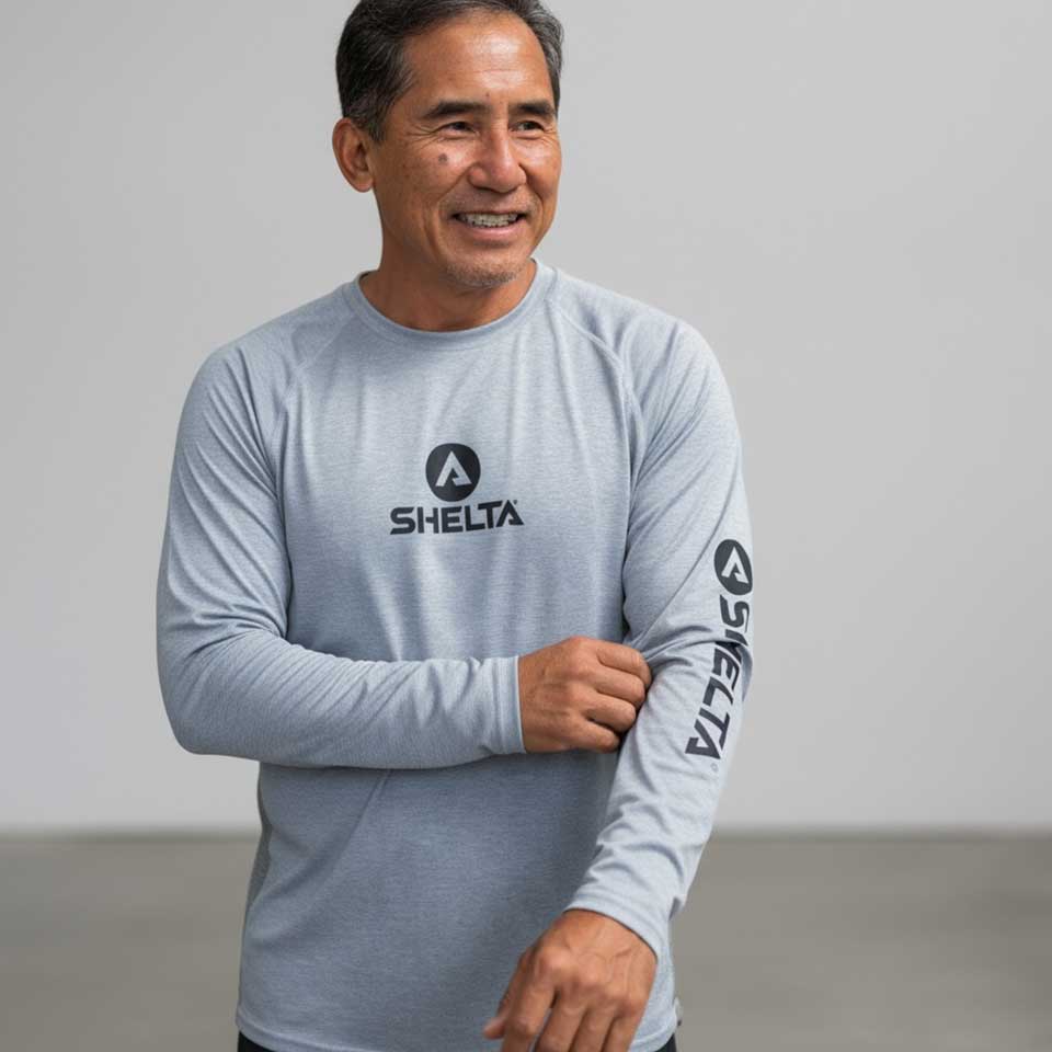 Man wearing a light blue long-sleeve shirt with 'SHELTA' branding on a gray background