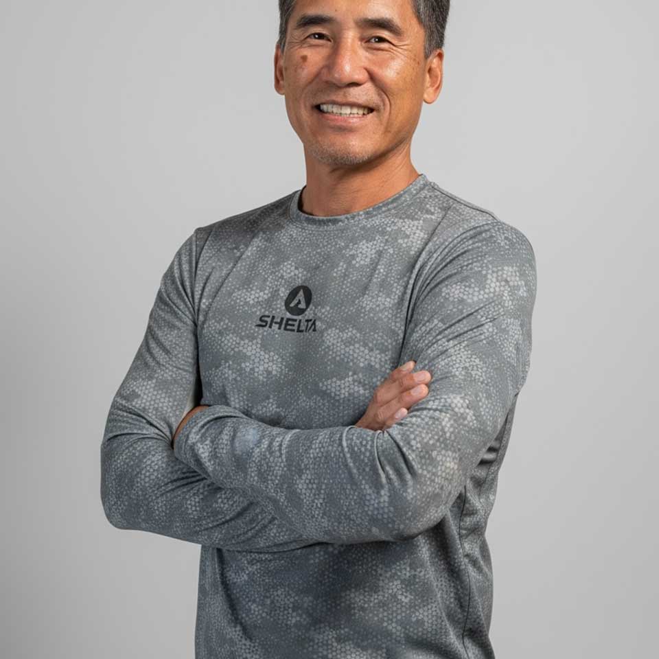 Man wearing a gray long-sleeve shirt with a shelta  brand logo on a gray background