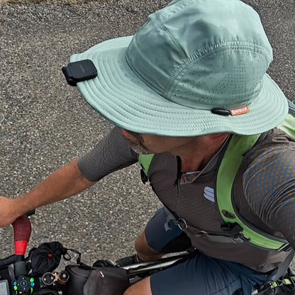 Person wearing a green bucket hat and cycling outfit, sitting on a bicycle.