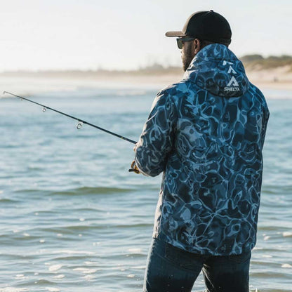 Man fishing by a body of water wearing a blue camouflage jacket.