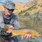 Person holding a large fish by a lake with mountains in the background