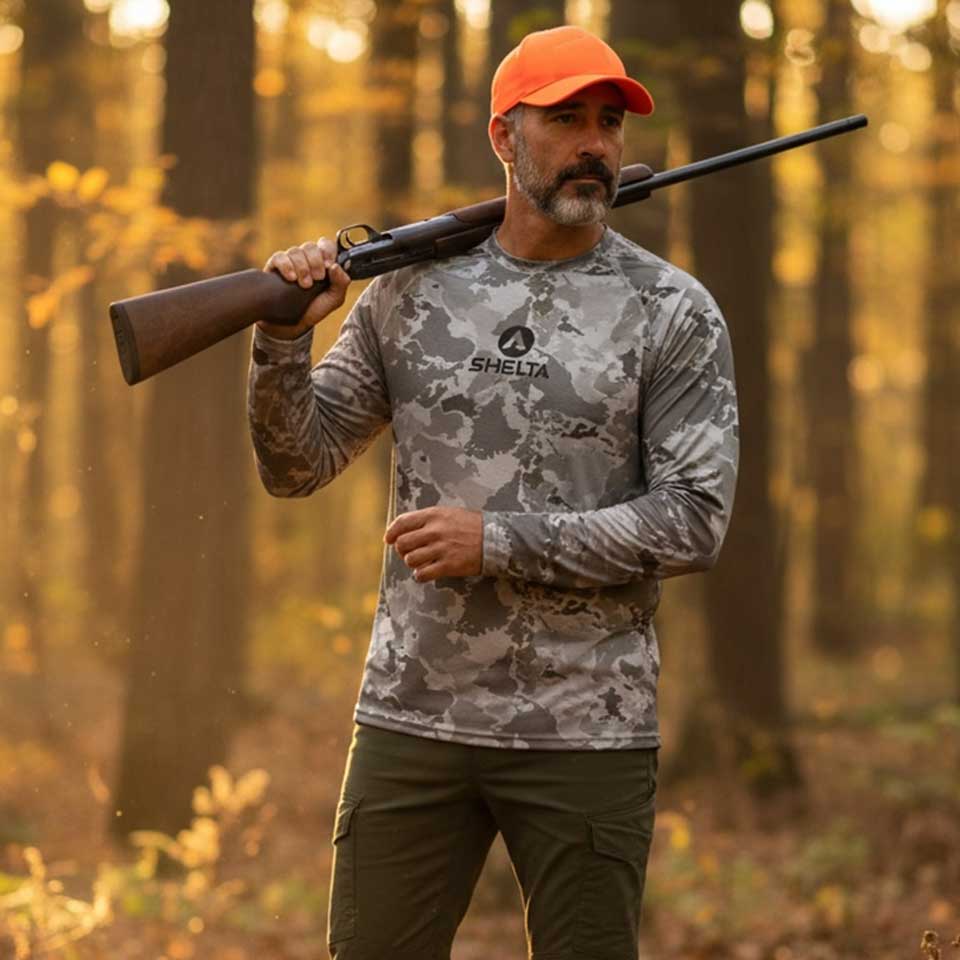 Man in camouflage shirt and orange cap holding a rifle in a forest setting