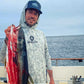 Man holding a large fish on a boat with ocean in the background