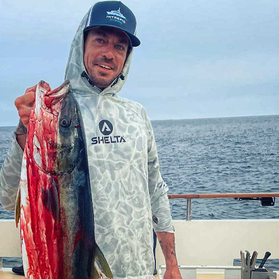 Man holding a large fish on a boat with ocean in the background