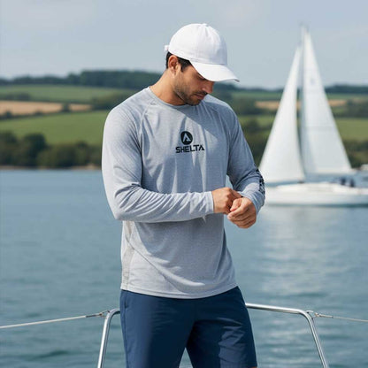 Man wearing a gray shirt with a logo on a boat with a sailboat in the background.