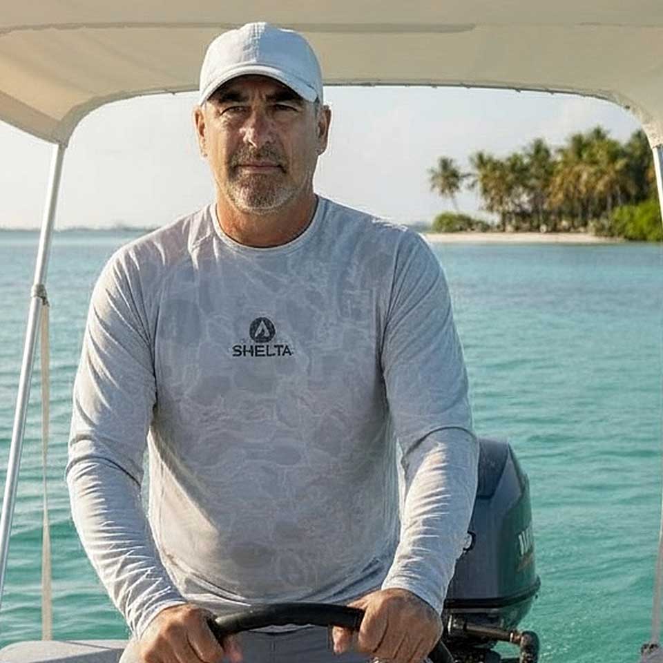 Man on a boat wearing a Shelta shirt with a scenic background