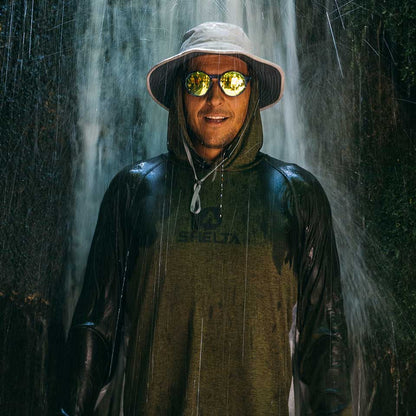 Person wearing a Shelta sun shirt and sunglasses standing in front of a waterfall