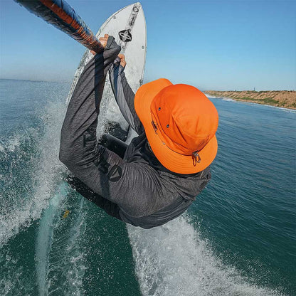 Person paddle boarding in the ocean wearing an orange hat and gray jacket.