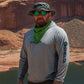 Man wearing a gray shirt with Selta logo, green bandana, and sunglasses in a desert landscape