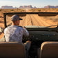 Person driving an open-top vehicle through a desert landscape with large rock formations.