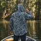 Person wearing a patterned jacket on a boat by a forested lake