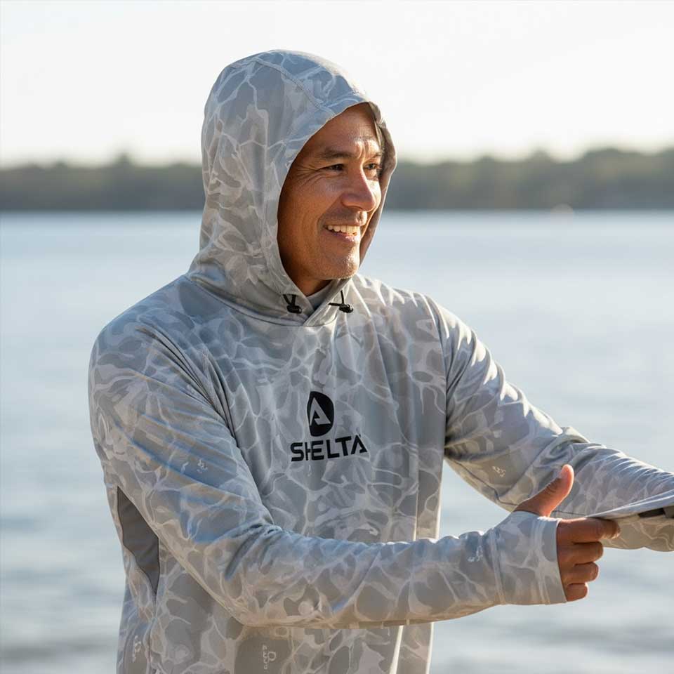 Person wearing a hooded shirt with 'Selta' branding by a body of water.