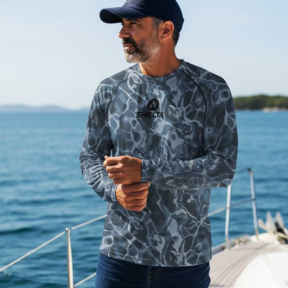 Man wearing a camouflage-patterned shirt with a brand logo, standing on a dock by the water.