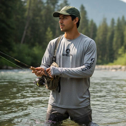 Man fishing in a river with trees and mountains in the background