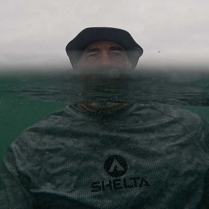 Person wearing a Shelta sun shirt and cap underwater with a foggy background