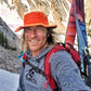 Person with skis on a mountain wearing an orange hat and red backpack
