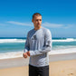 Man wearing a gray long-sleeve shirt with a logo on a beach