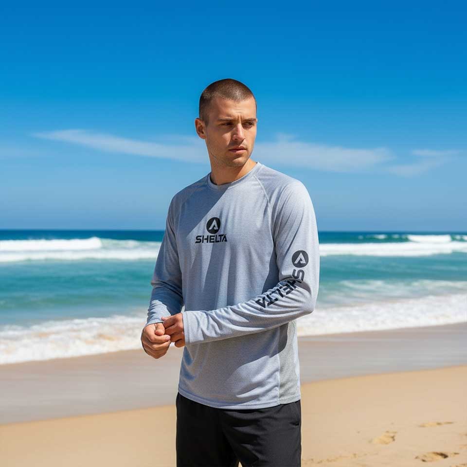 Man wearing a gray long-sleeve shirt with a logo on a beach