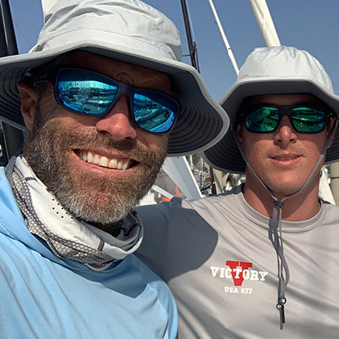 Two men wearing hats and sunglasses on a boat, with one wearing a 'Victory' shirt.