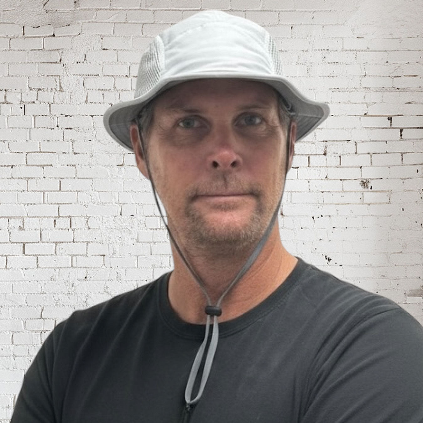 Man wearing a white bucket hat against a white brick wall