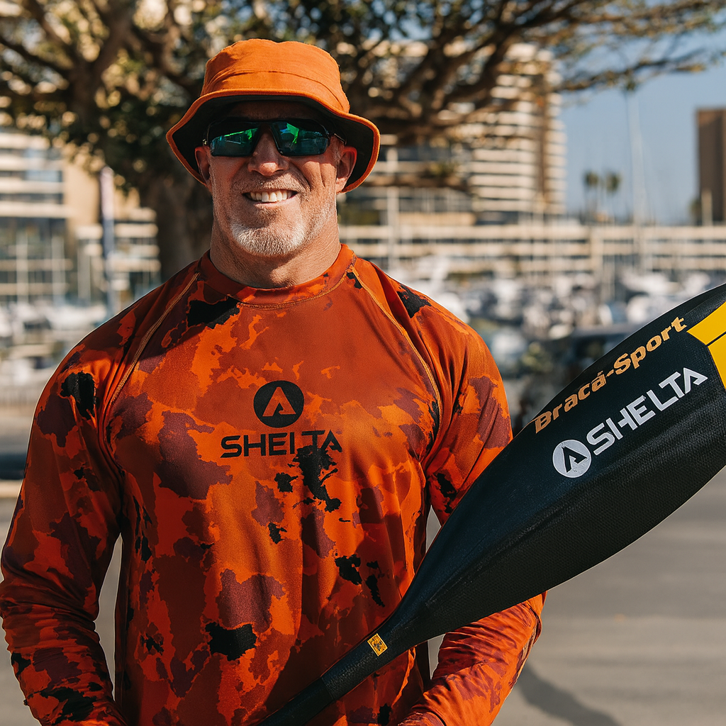 Man wearing an orange shirt and hat, holding a paddle with Selta branding, outdoors.