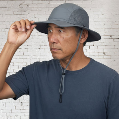 Man wearing a gray bucket hat against a white brick wall.