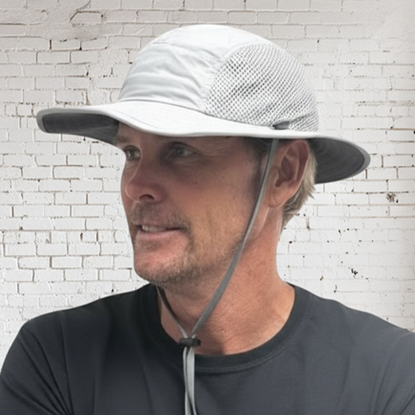 Man wearing a wide-brimmed hat with a white brick wall background