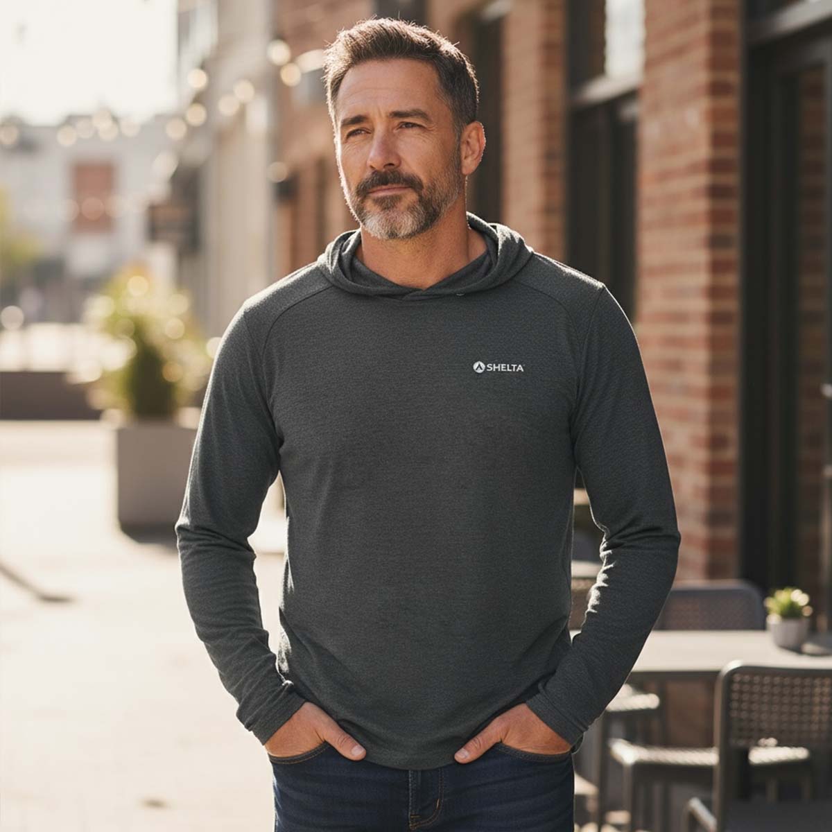 Man wearing a dark gray hoodie with a logo, standing outdoors.